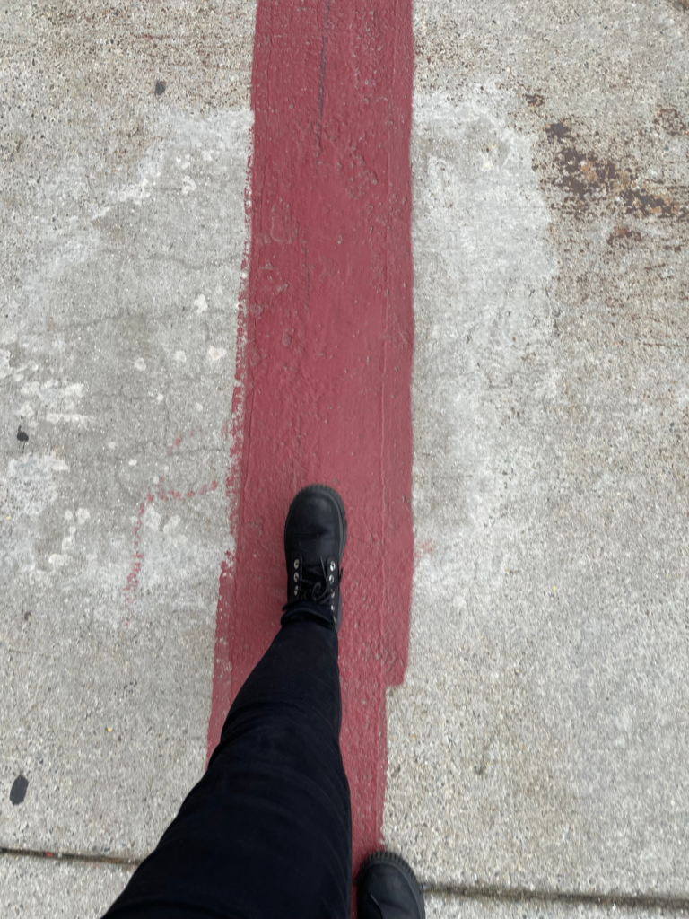 A woman wearing black jeans and black boots on a 3-day Boston itinerary walking on a painted red line marking the Freedom Trail.